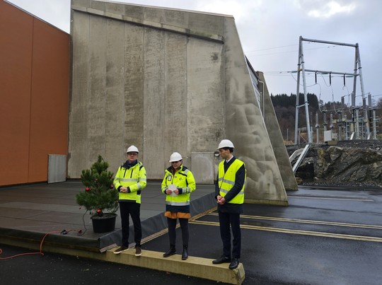 Eimund Nygaard, Marianne Frøystad Ånestad og Andreas Bjelland Eriksen foran transformatorstasjon i grå og mørk oransje betong. 