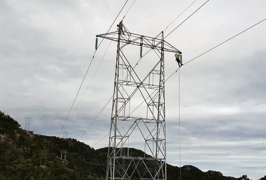 To montører i toppen av en strømmast for å bytte deler i forbindelse med bytte av linetråd.