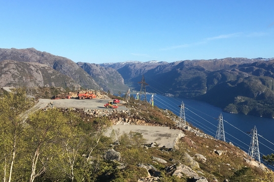 På en høyde over fjorden står strømmaster til fjordspenn. Like ved er det gruset opp anleggsplass til bygging av ny kraftlinje.