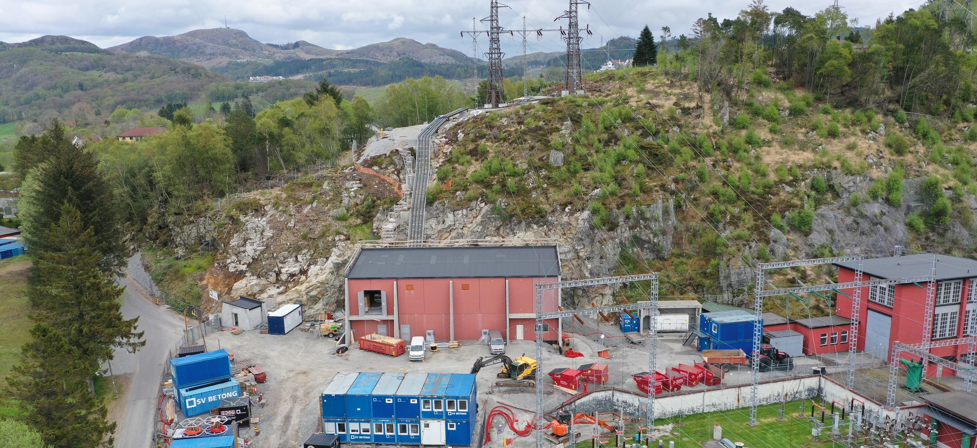 Tronsholen transformatorstasjon med nytt bygg i bakkant inn mot fjellsiden til venstre for det gamle bygget. 