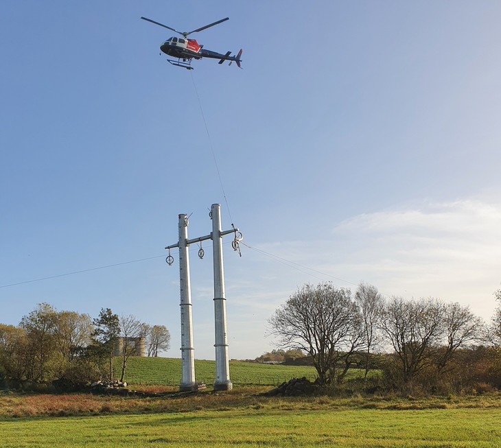 Helikopter strekker linetråd ved lysegrå mast i forbindelse med bygging av ny kraftledning på Jæren