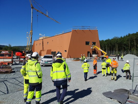 Prosjektgruppen i gule jakker og hjelm på befaring ved Veland transformatorstasjon som bygges i brunoransje betong.
